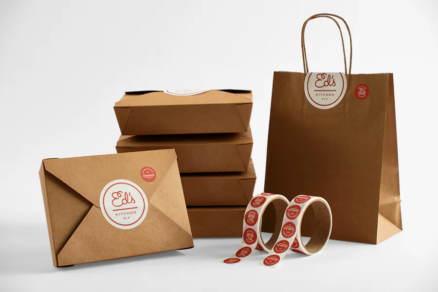 Takeout boxes and bags sealed with custom labels with a round design and Ed's Kitchen SLP in red.