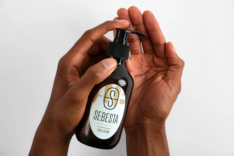 Two hands holding a bottle of lotion with an oval label printed with Sebesta Apothecary Shea Lotion.