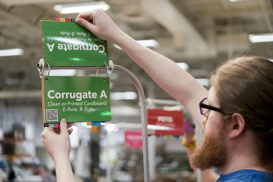 A man in a production area standing by a recycling bin with a flip book printed with Corrugate A.