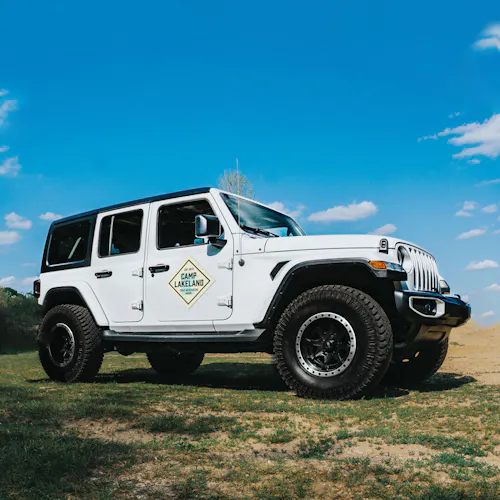 A white jeep parked in a grassy spot with a car magnet on the passenger door.