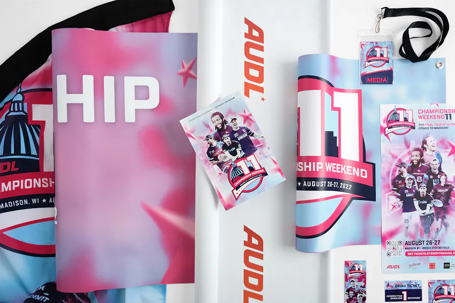 Print marketing materials for AUDL, including a feather flag, hanging banners, a lanyard, event tickets and a program.