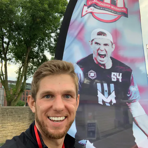 A man smiling and standing in front of a feather flag printed with an image of him and AUDL Championship Weekend 11.