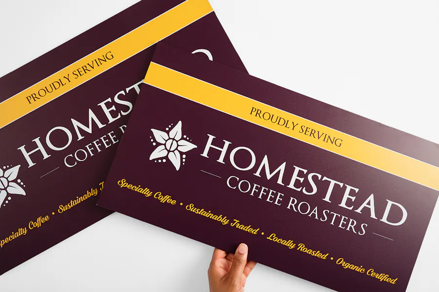 A hand holding a custom aluminum sign printed with Proudly Serving Homestead Coffee Roasters.