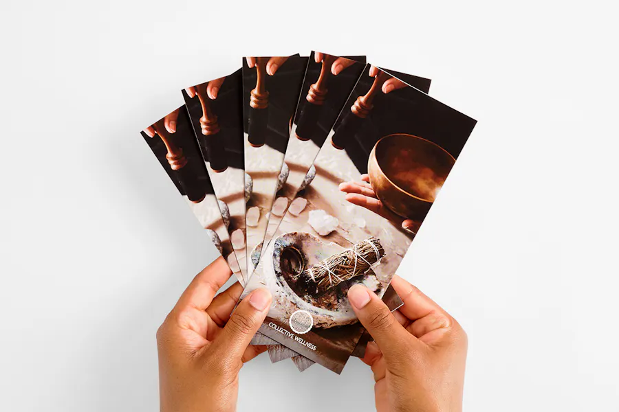 Two hands holding five fanned-out brochures printed with Collective Wellness, incense and crystals on the cover.