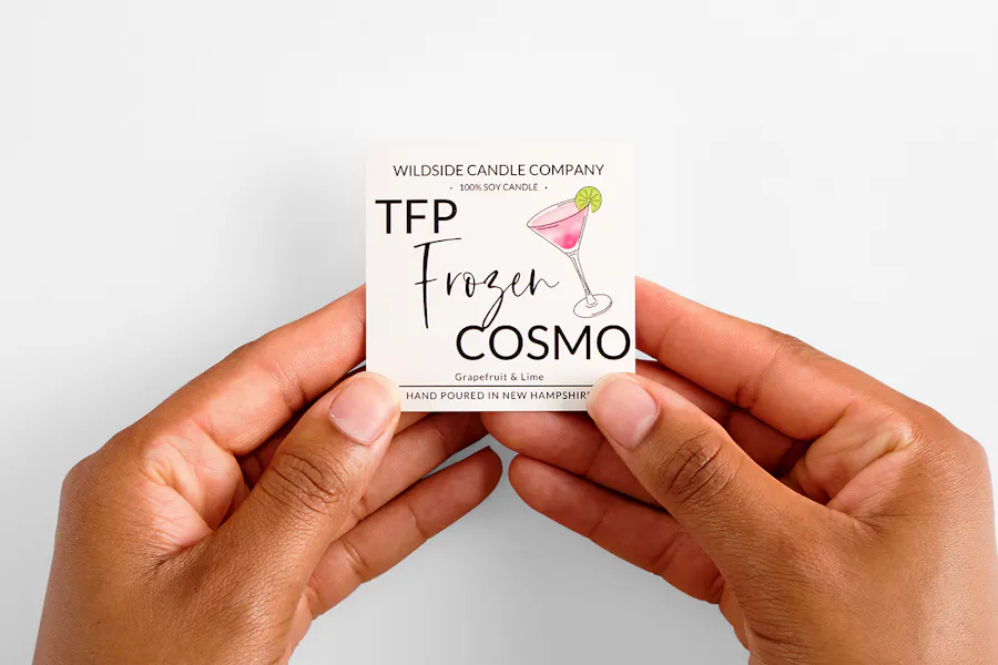Two hands holding a custom square label printed with Wildside Candle Company TFP Frozen Cosmo.