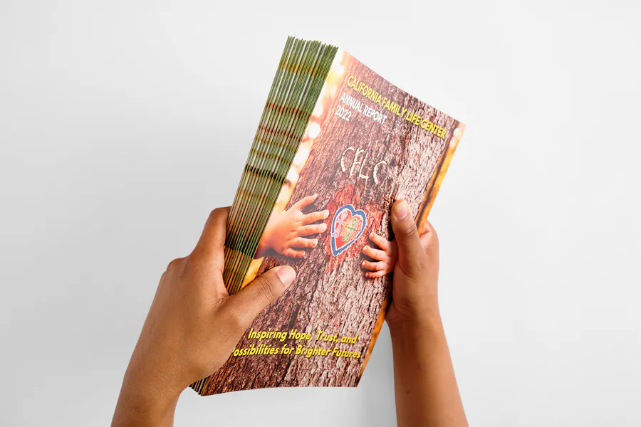 Two hands holding a stack of booklets printed with California Family Life Center Annual Report 2022.