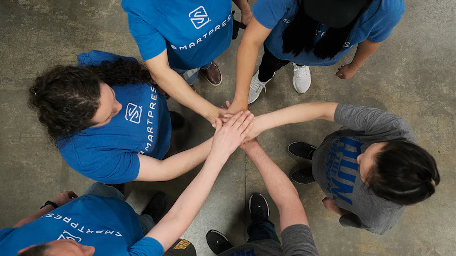 A group of people wearing Smartpress T-shirts standing in a circle with their hands in the middle.