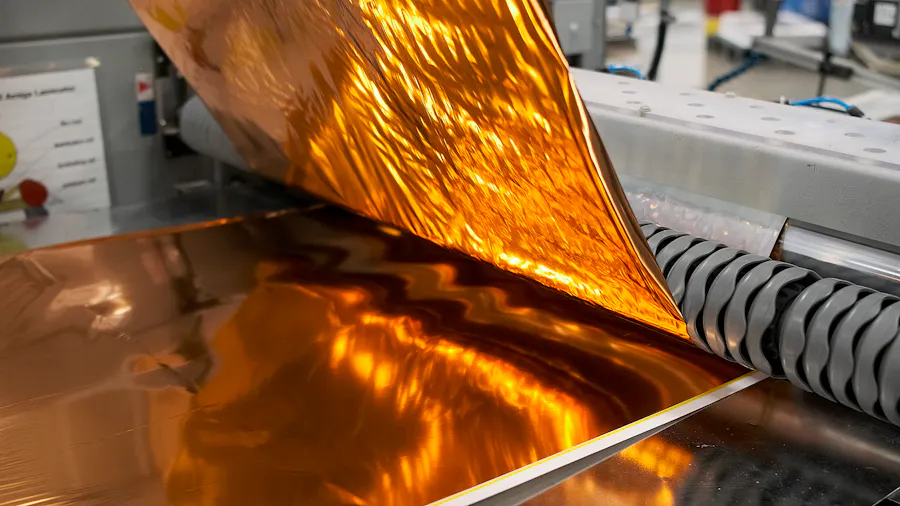 Gold foil being applied to a booklet cover through a machine in a printing production facility.