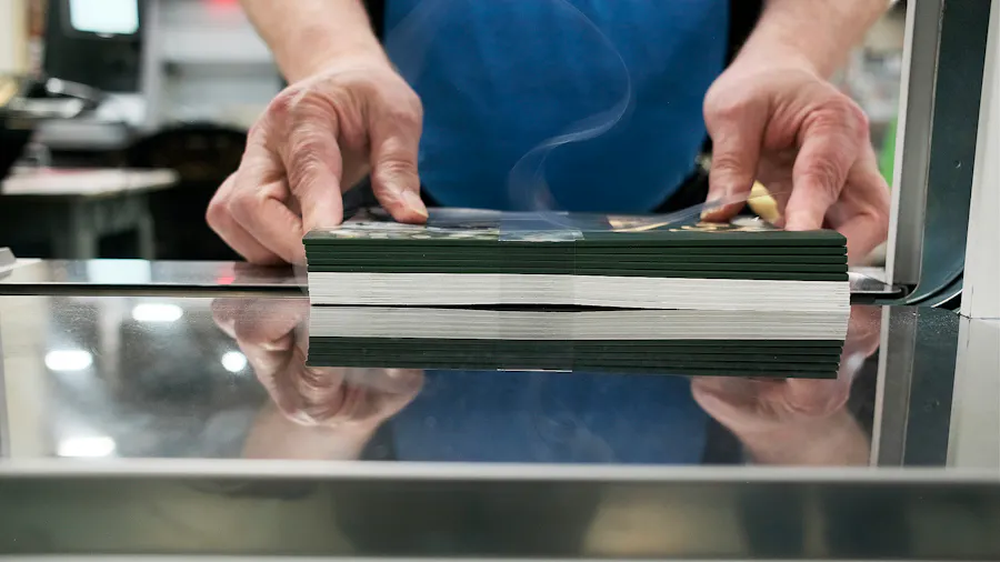 Two hands holding a stack of custom printed booklets as it gets two plastic belly bands wrapped around it on a machine in a production facility.