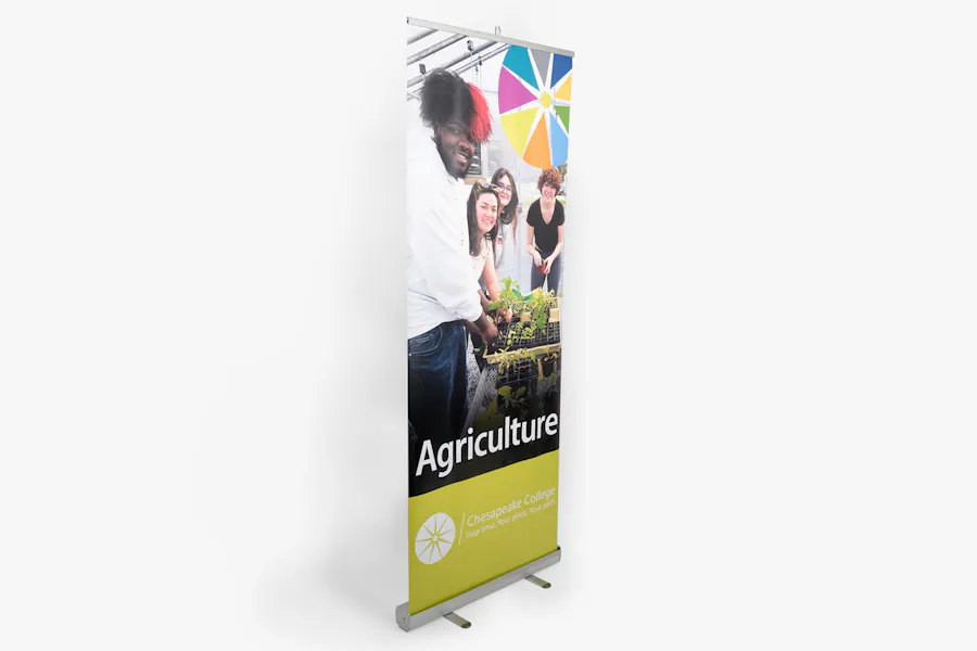 A retractable banner printed with four people smiling and standing over plants with Agriculture in white below them.