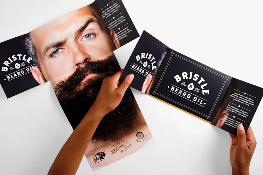 Two hands holding open a T-cross mailer over another mailer unfolded to an image of a man with a long beard.