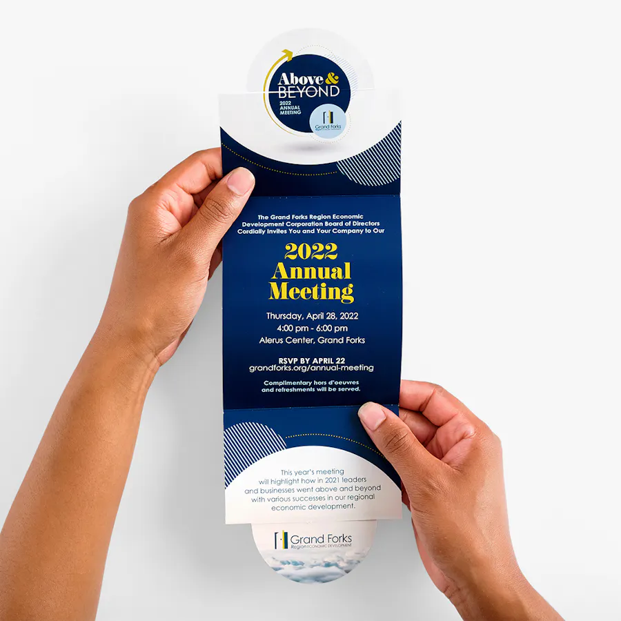 Two hands holding open a gate fold brochure printed with Above & Beyond and 2022 Annual Meeting.