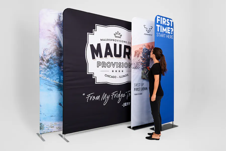 A woman standing in front of four tension fabric displays in different sizes printed with various marketing designs.