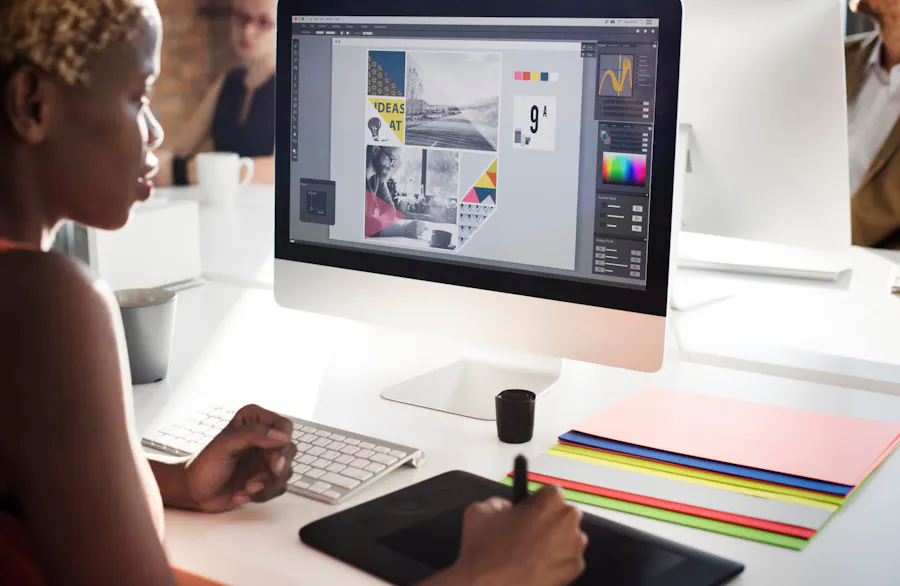 A woman sitting at a desk designing a marketing asset on a desktop computer.