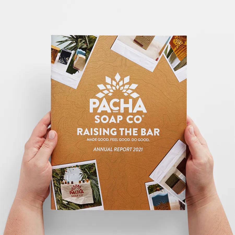 Two hands holding a Pacha Soap Co. annual report with Raising the Bar printed on the cover.