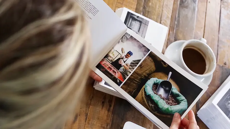 A woman flipping through a marketing booklet while sitting at a wooden table with a cup of coffee next to her.