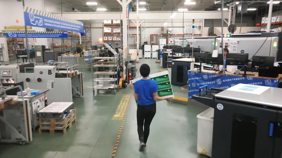 A production facility for an online printer with a person wearing a blue shirt walking between presses and other machinery.