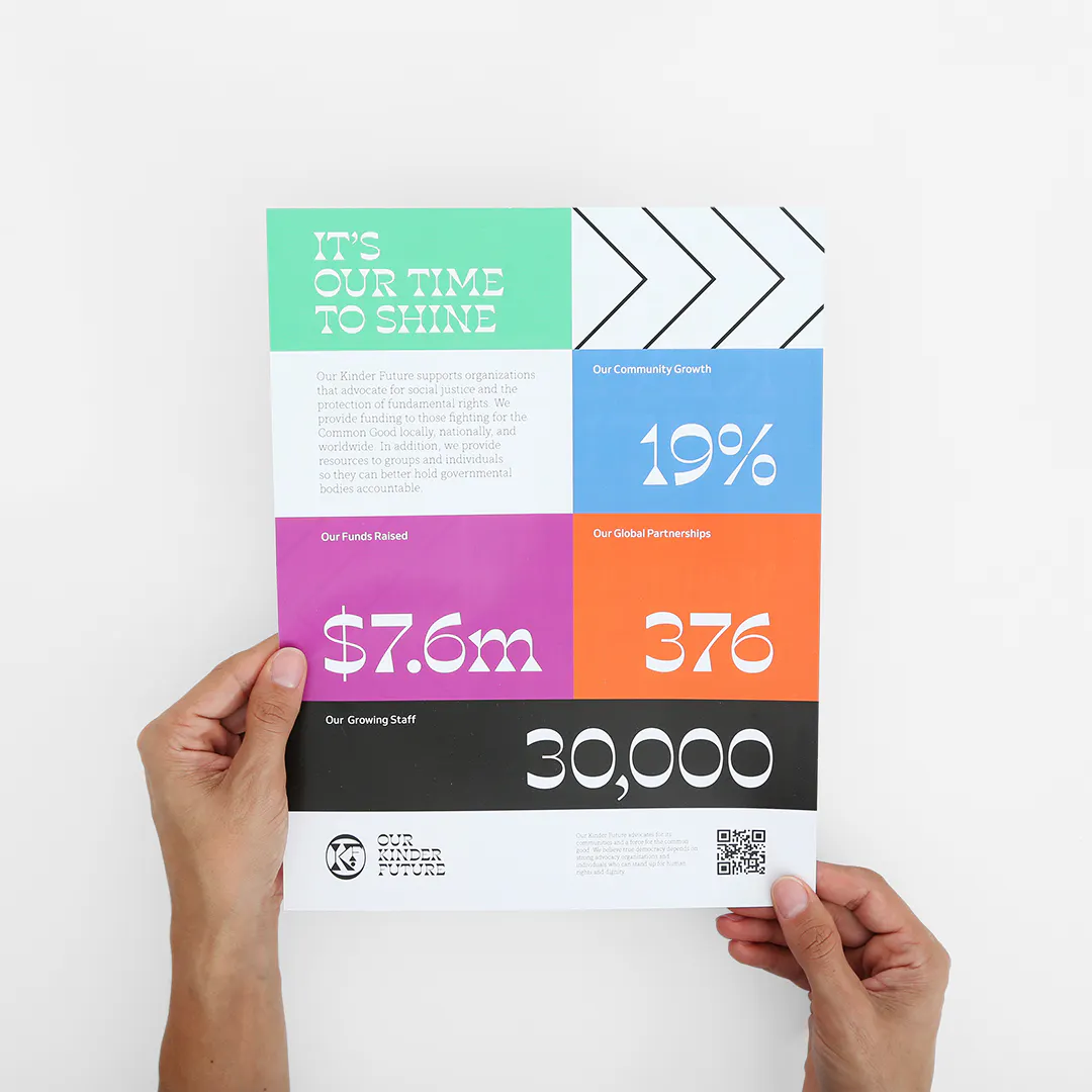 Two hands holding a custom flyer printed with a green, blue, orange, pink and black design and a QR code in the bottom corner.