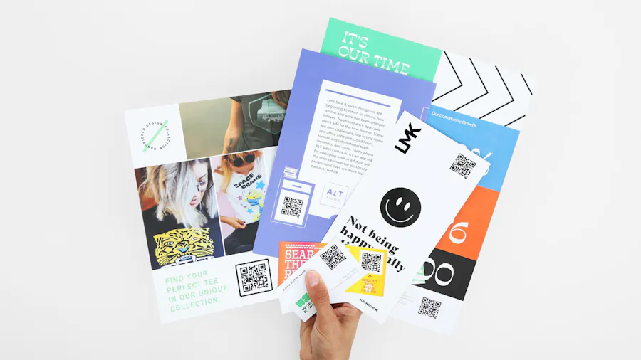 A hand holding an array of fanned-out print marketing pieces printed with bright colors and QR codes.