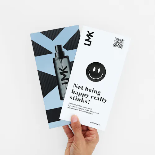 A hand holding two fanned-out postcards printed with an image of a perfume bottle and a QR code in the corner.