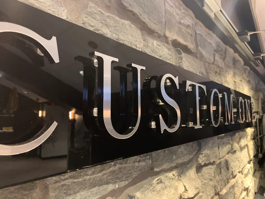 A black acrylic sign printed with Custom One in silver lettering hanging on a stone wall.