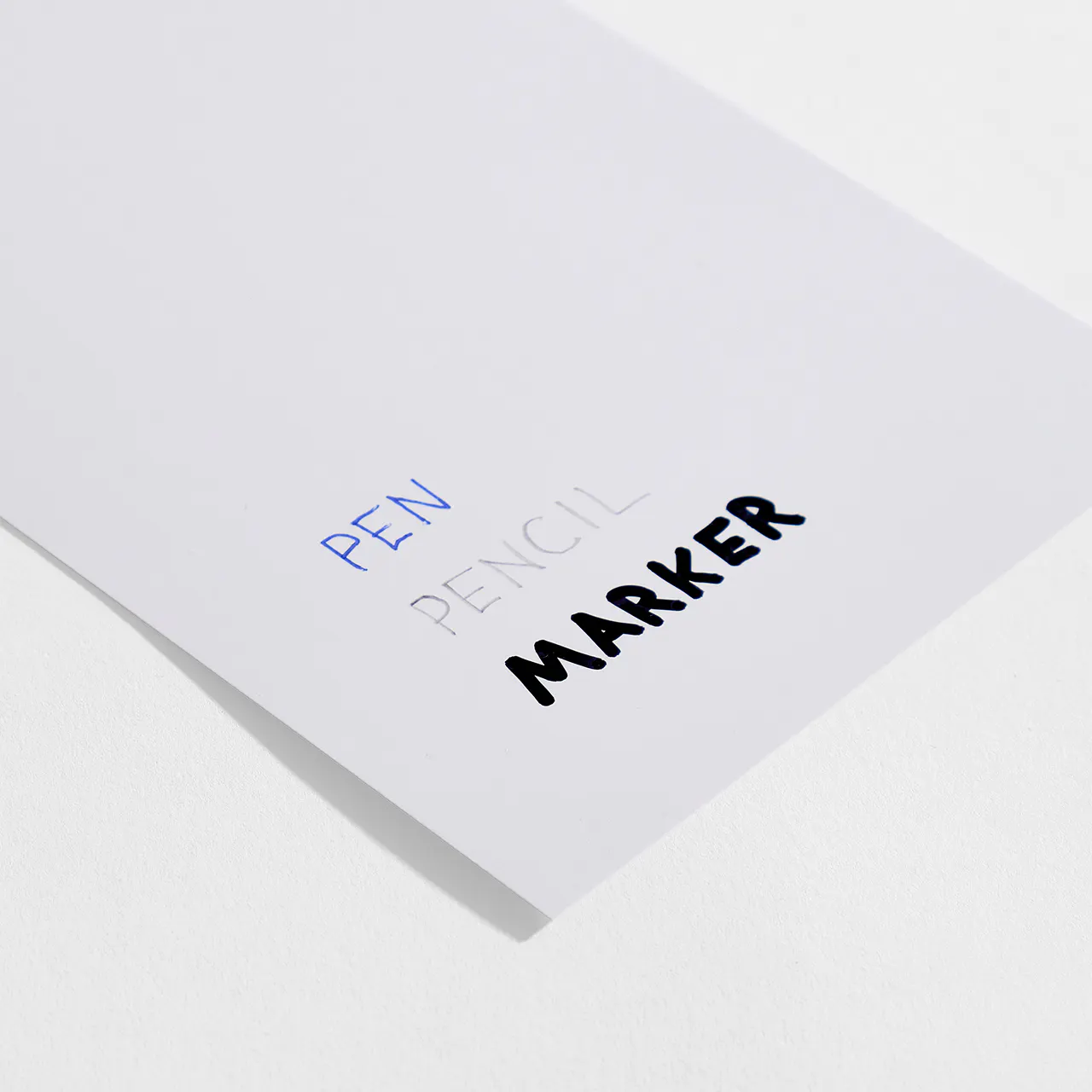 Coated gloss paper stock with pen, pencil and marker written on it.