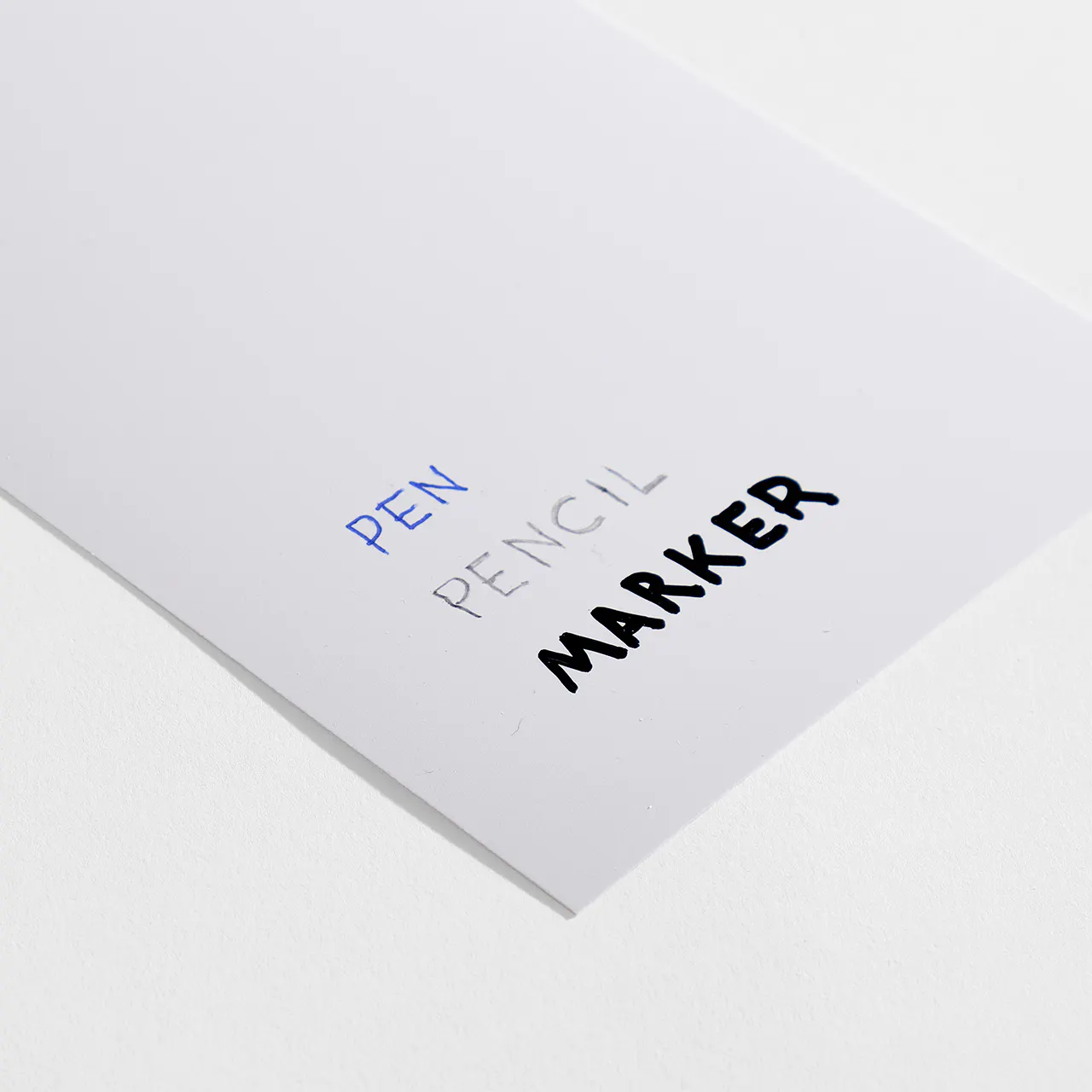 Coated matte paper stock with pen, pencil and marker written on it.