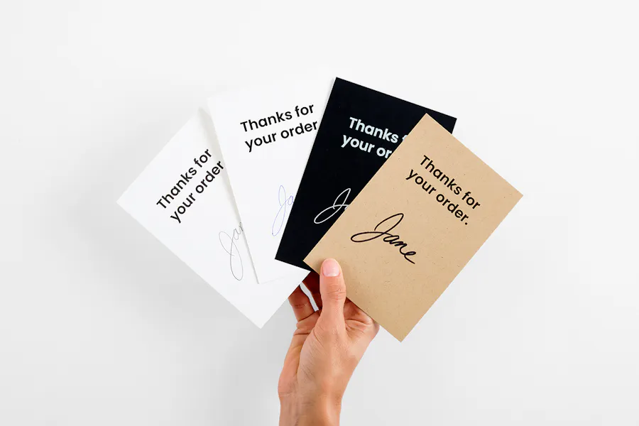 A hand holding four fanned-out product inserts printed with Thanks for your order and a handwritten name.