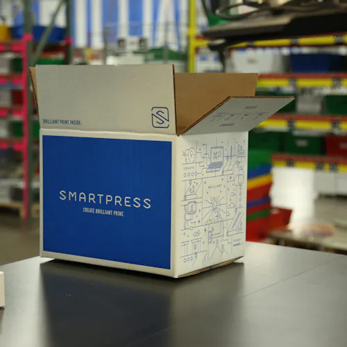 A sustainable packaging box printed with Smartpress branding sitting on a table in a production facility.