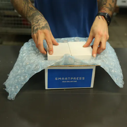 Two hands putting a product into a sustainable packaging box printed with Smartpress on the side.
