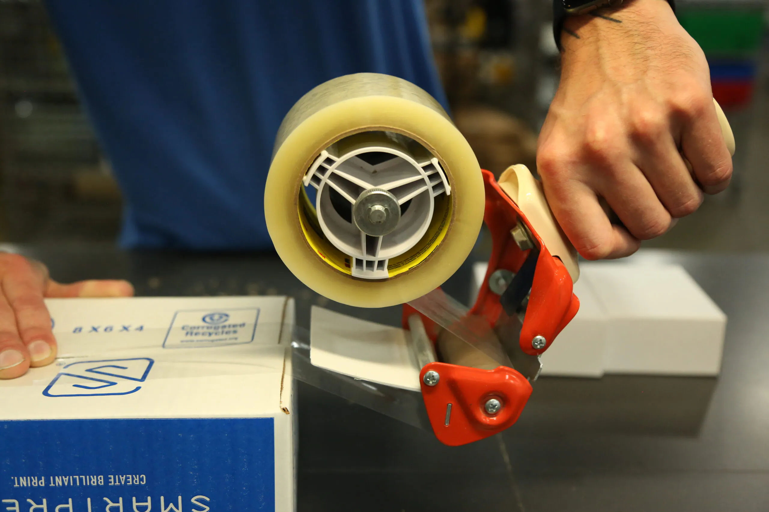 Two hands taping a sustainable packaging box closed in a production facility.