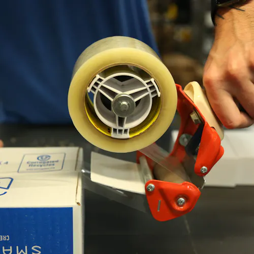 Two hands taping a sustainable packaging box closed in a production facility.