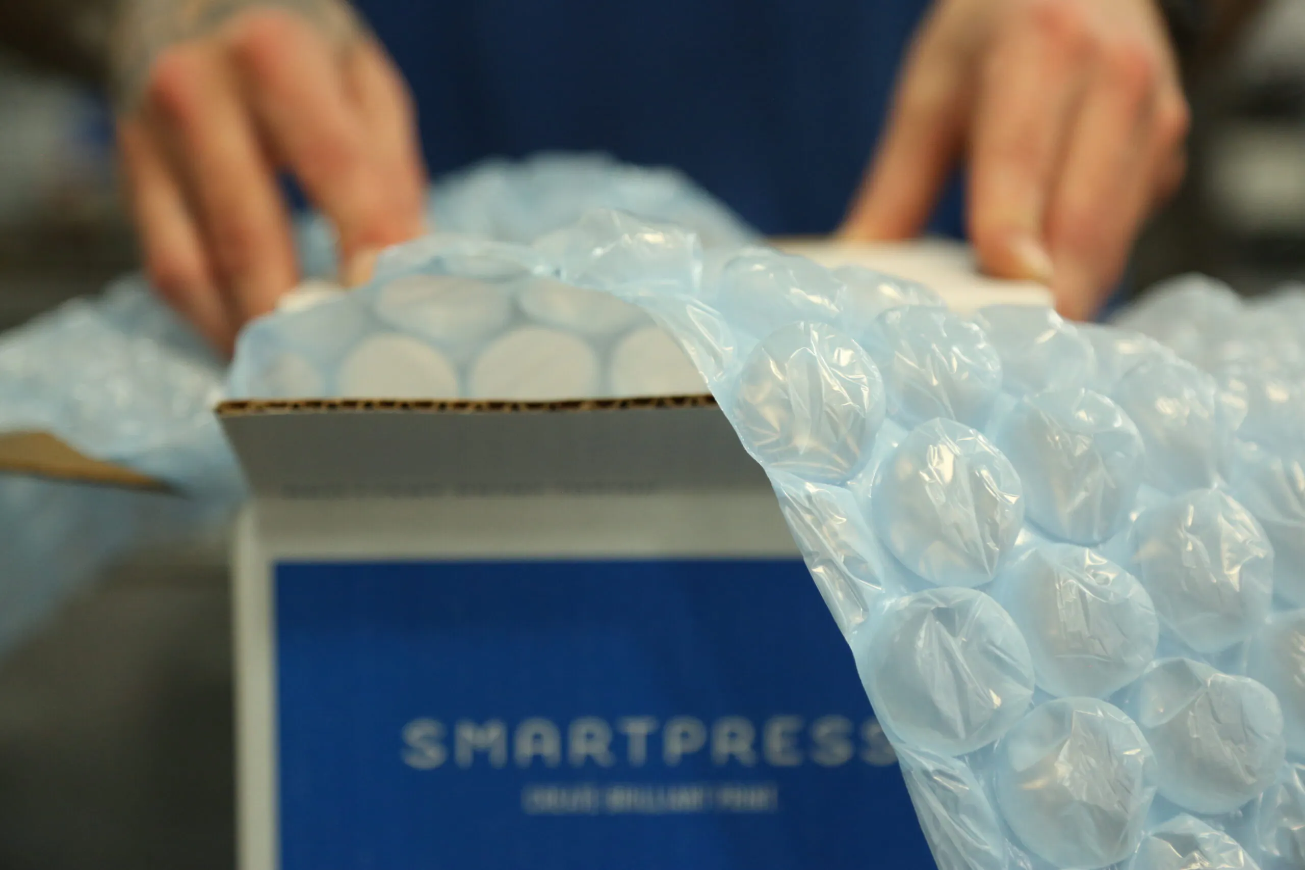 Bubble wrap coming out of and draping over the side of a sustainable packaging box printed with Smartpress.