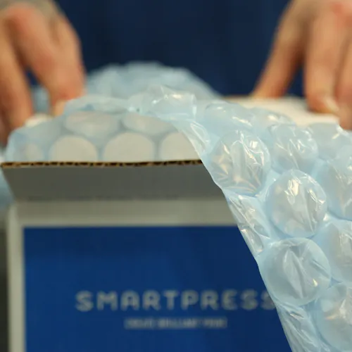 Bubble wrap coming out of and draping over the side of a sustainable packaging box printed with Smartpress.