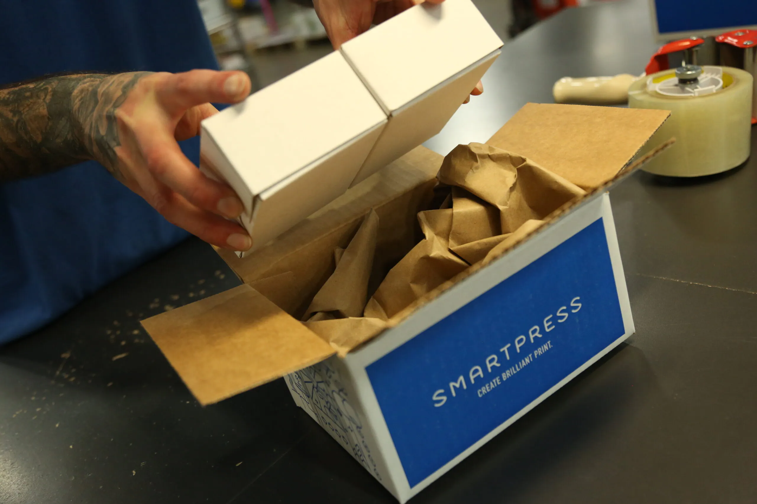 Two hands holding a white product box above a sustainable packaging box printed with Smartpress on the side.