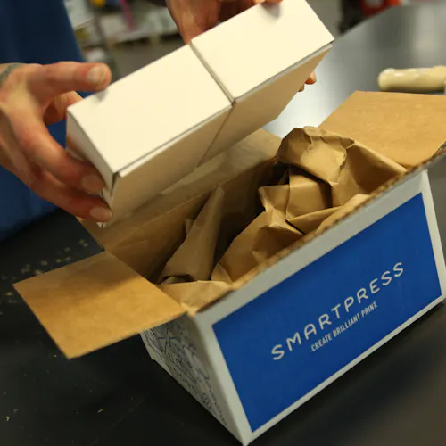 Two hands holding a white product box above a sustainable packaging box printed with Smartpress on the side.