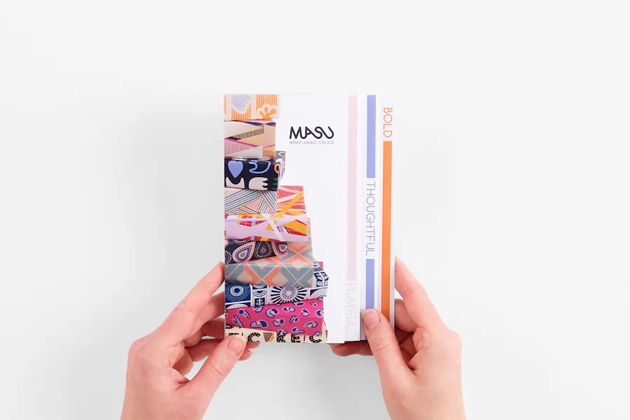 Two hands holding a stepped accordion brochure printed with Masu Wrap Hand Create.