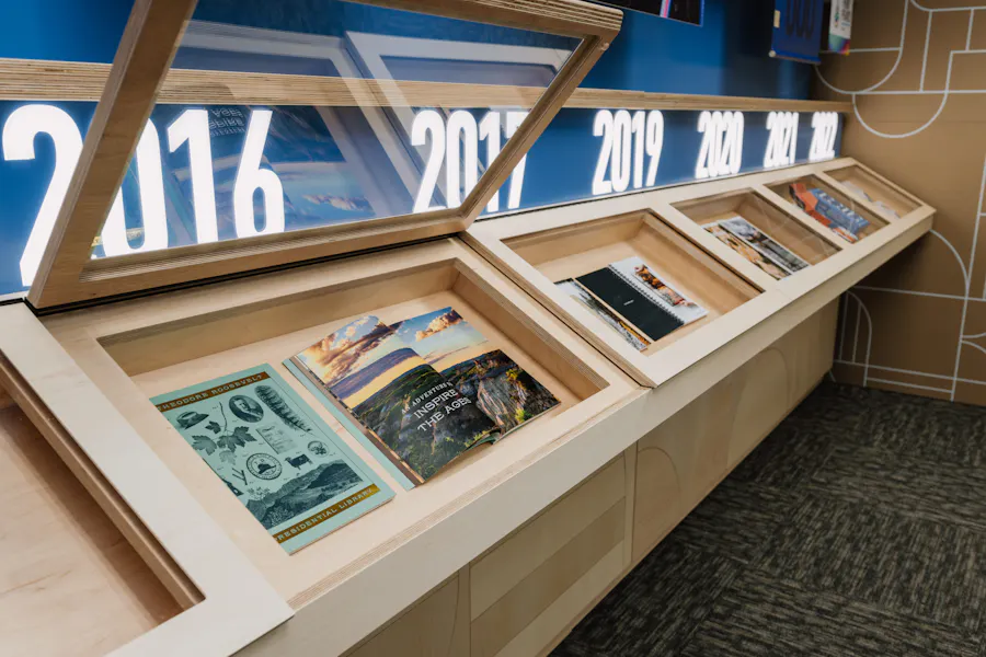 A custom wooden display case with shelves holding printed booklets underneath backlit dates.