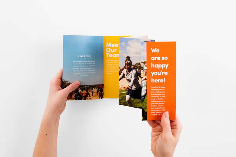 Two hands unfolding an accordion brochure printed with a bright blue, yellow and orange design.