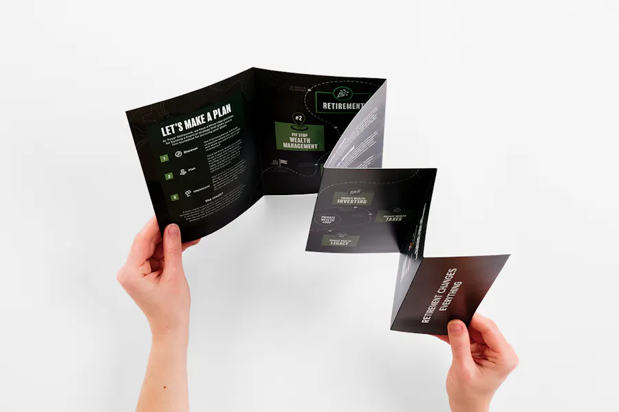 Two hands unfolding an accordion fold brochure printed with retirement details and a green and black design.