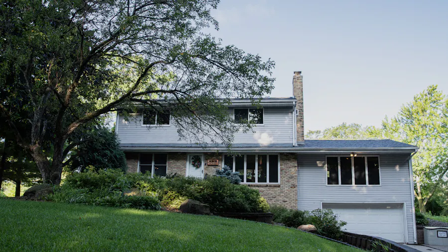 A two-story house with brick and white siding, dark green bushes in front of it and a sign that says Hope House by the front door.