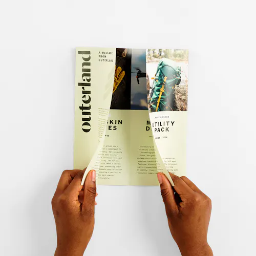 Two hands unfolding a closed gate brochure printed with Outerland and outdoor gear details.