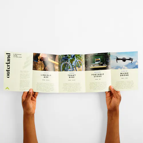Two hands holding a roll fold brochure printed with five panels and outdoor gear details.