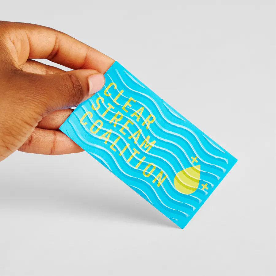 A hand holding a raised UV business card printed with a blue and yellow design and Clear Stream Coalition.