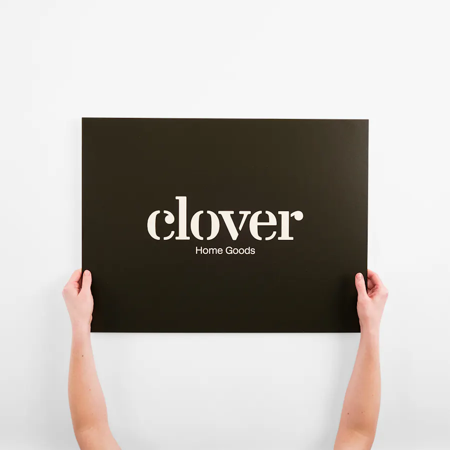 Two hands holding a custom eco-friendly sign printed with Clover Home Goods in white.