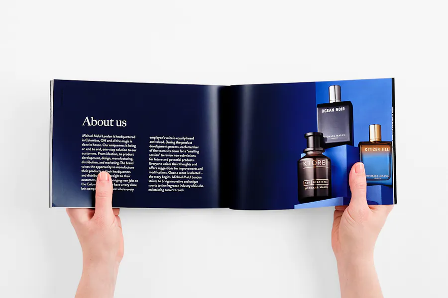 Two hands holding open a perfect bound book printed with a lookbook design for fragrance brand.