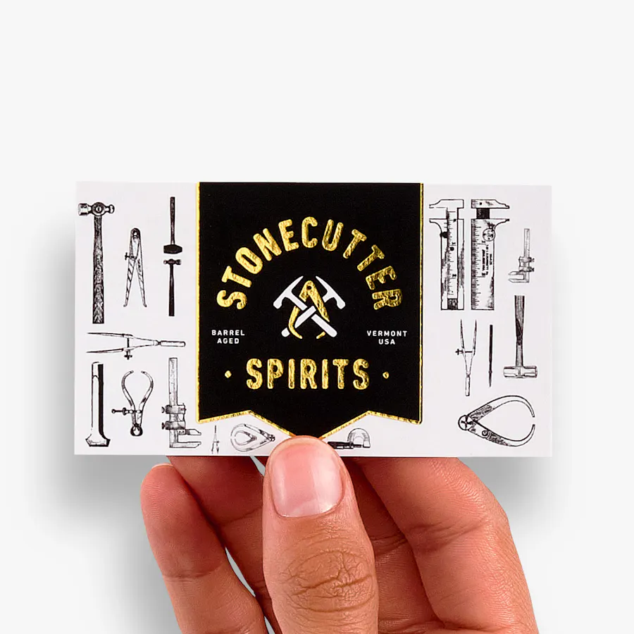 A hand holding a foil business card printed with Stonecutter Spirits in gold foil.