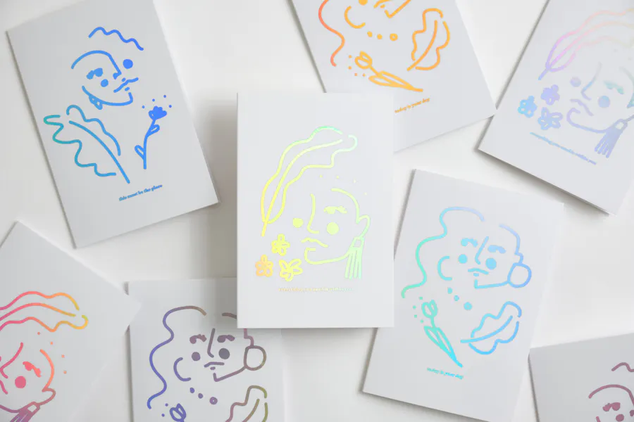 A collection of scattered greeting cards printed with a holographic foil illustration on the cover.