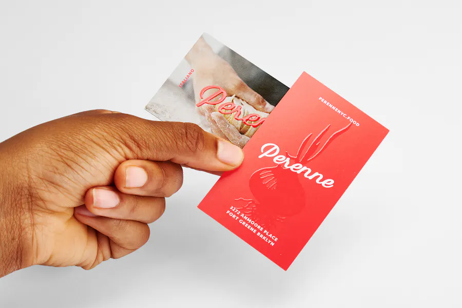 A hand holding two custom business cards printed with Perenne in white and red and finished with a raised UV coating.