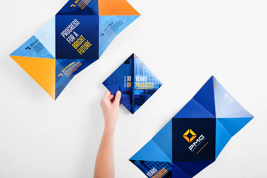 A hand holding a custom brochure printed with a tulip fold and a blue and orange design.